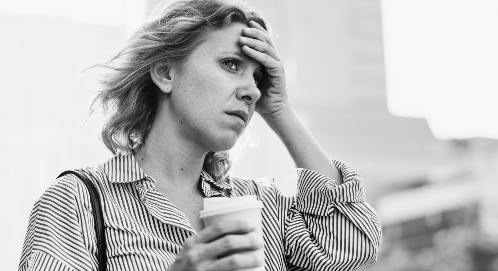 Mujer angustiada sosteniendo un café, imagen en blanco y negro que refleja ansiedad o estrés.