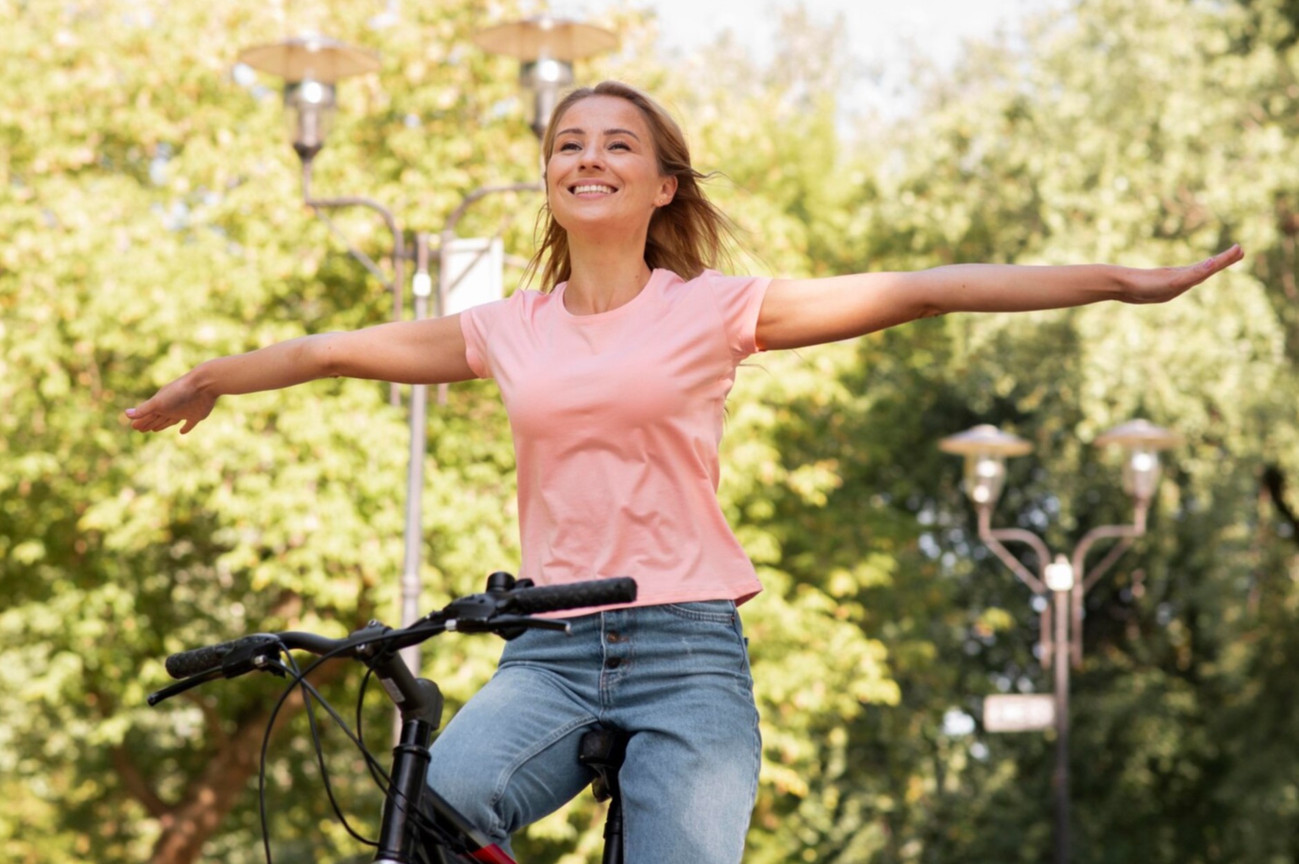 Mujer sonriendo con los brazos abiertos mientras monta en bicicleta, símbolo de bienestar emocional.