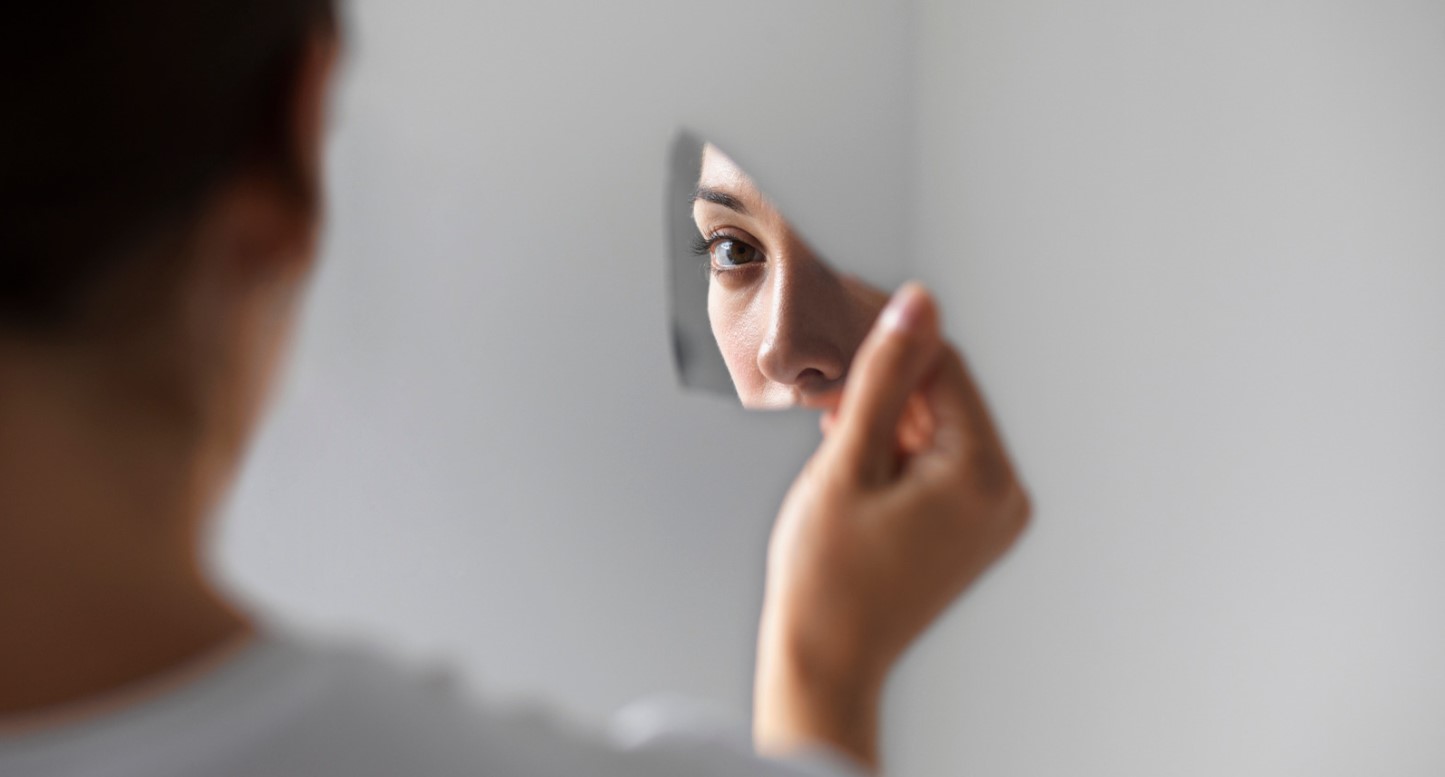 Persona reflexionando sobre sí misma en un trozo de espejo, representando el trabajo personal en la autoestima.