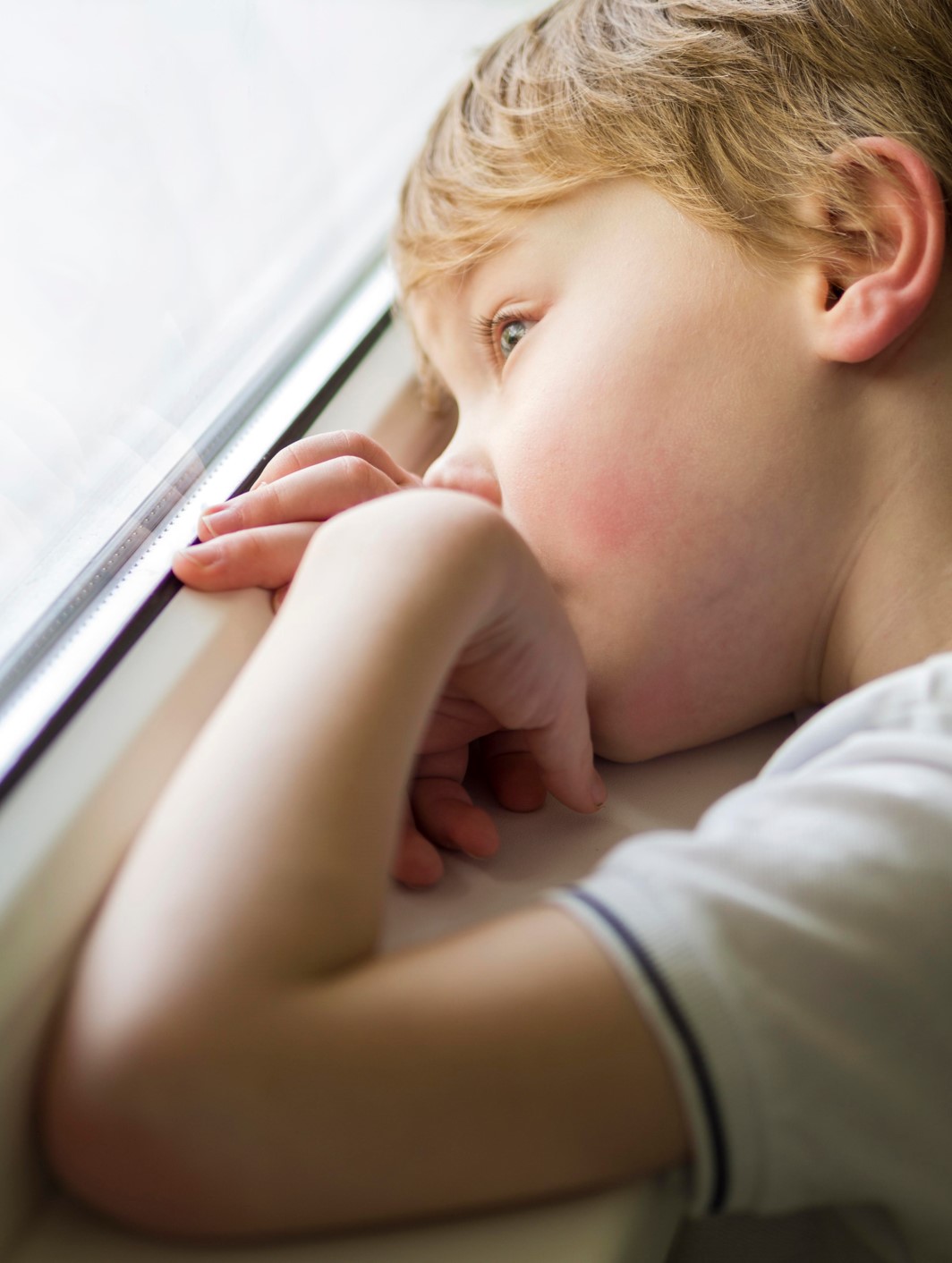 Niño apoyado junto a la ventana, evocando aislamiento o introspección típica en casos de Asperger.