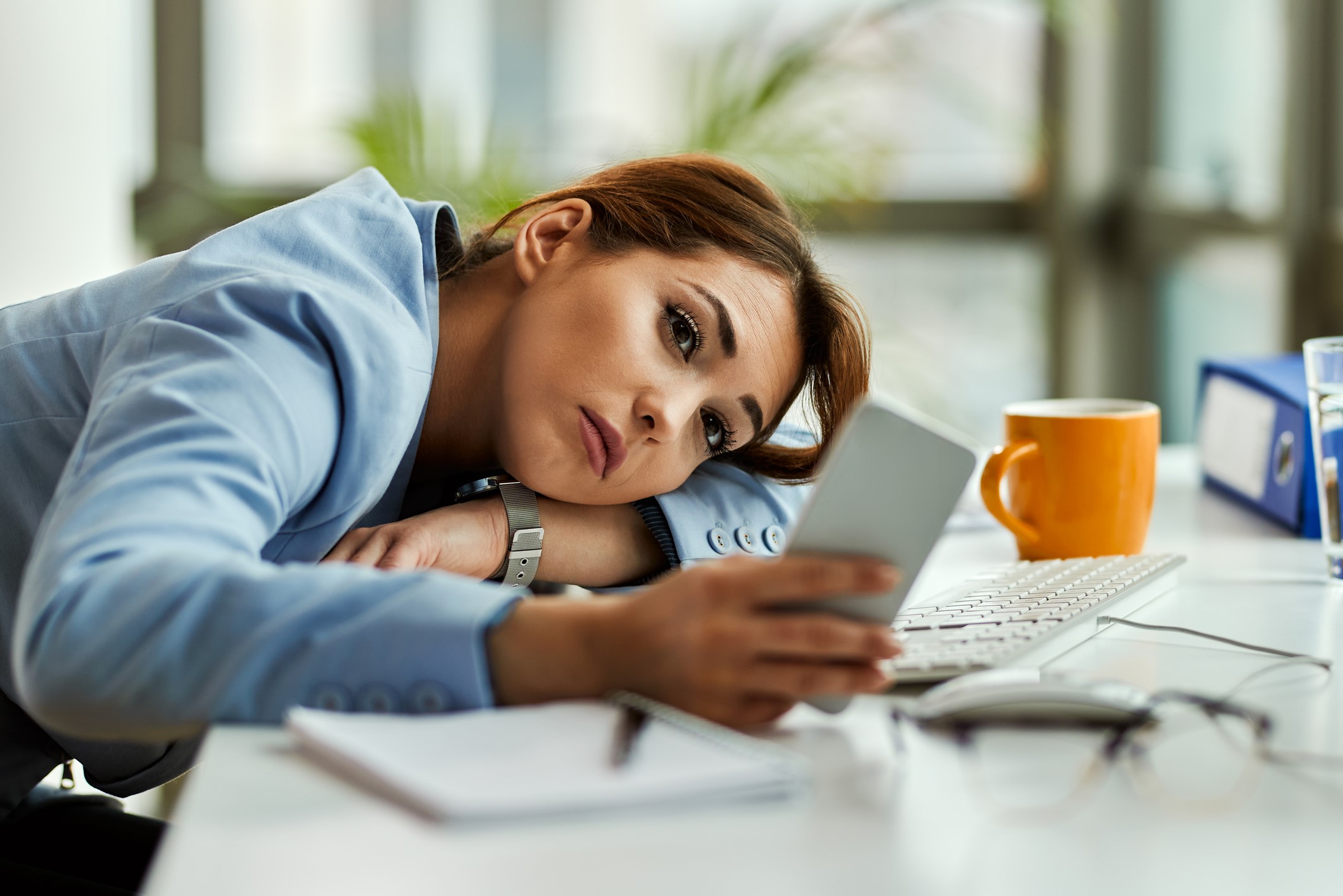 Mujer distraída en el trabajo mirando el móvil, ejemplo de procrastinación.