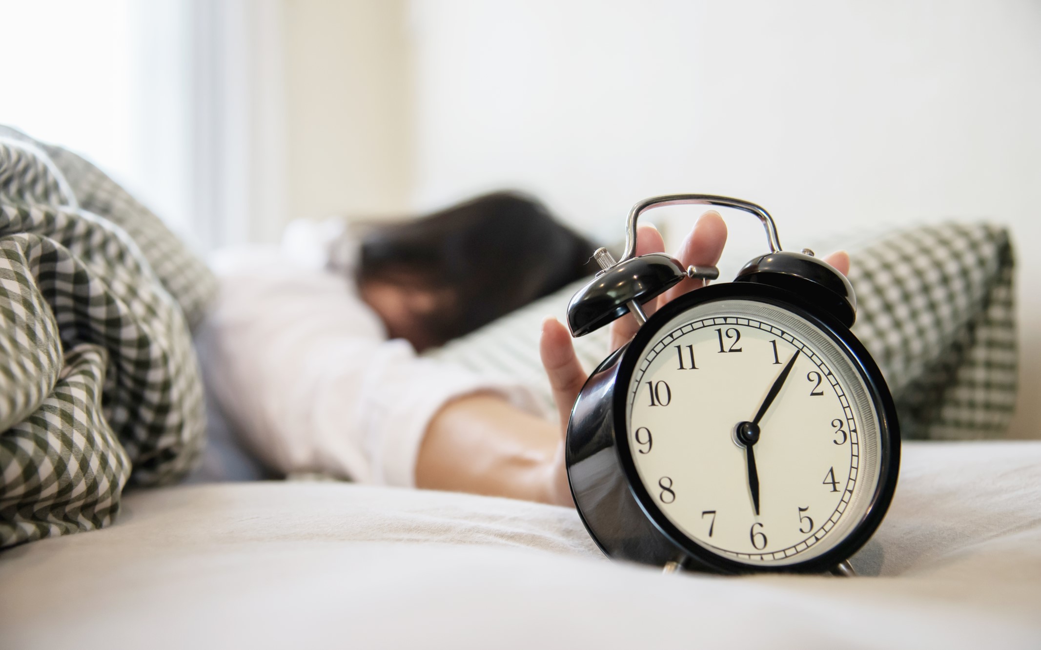 Persona apagando un reloj despertador en la vuelta a la rutina.